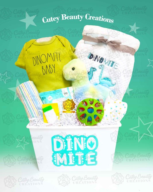 A dinosaur-themed baby basket from Cutey Beauty Creations, featuring a green background and containing various baby items like a plush toy, onesie, wipes, bib, and blanket.